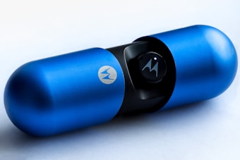 A blue, capsule-shaped object with a metallic finish and brand logo. The object appears to be a portable speaker, characterized by its sleek and modern design.