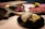 A luxurious and artistic food presentation featuring a black plate with a decorative, cream-colored bowl that is partially open to reveal gold leaf. The background displays a wooden serving board with slices of raw meat and garnishes, including flowers and herbs. The atmosphere is elegant and sophisticated.