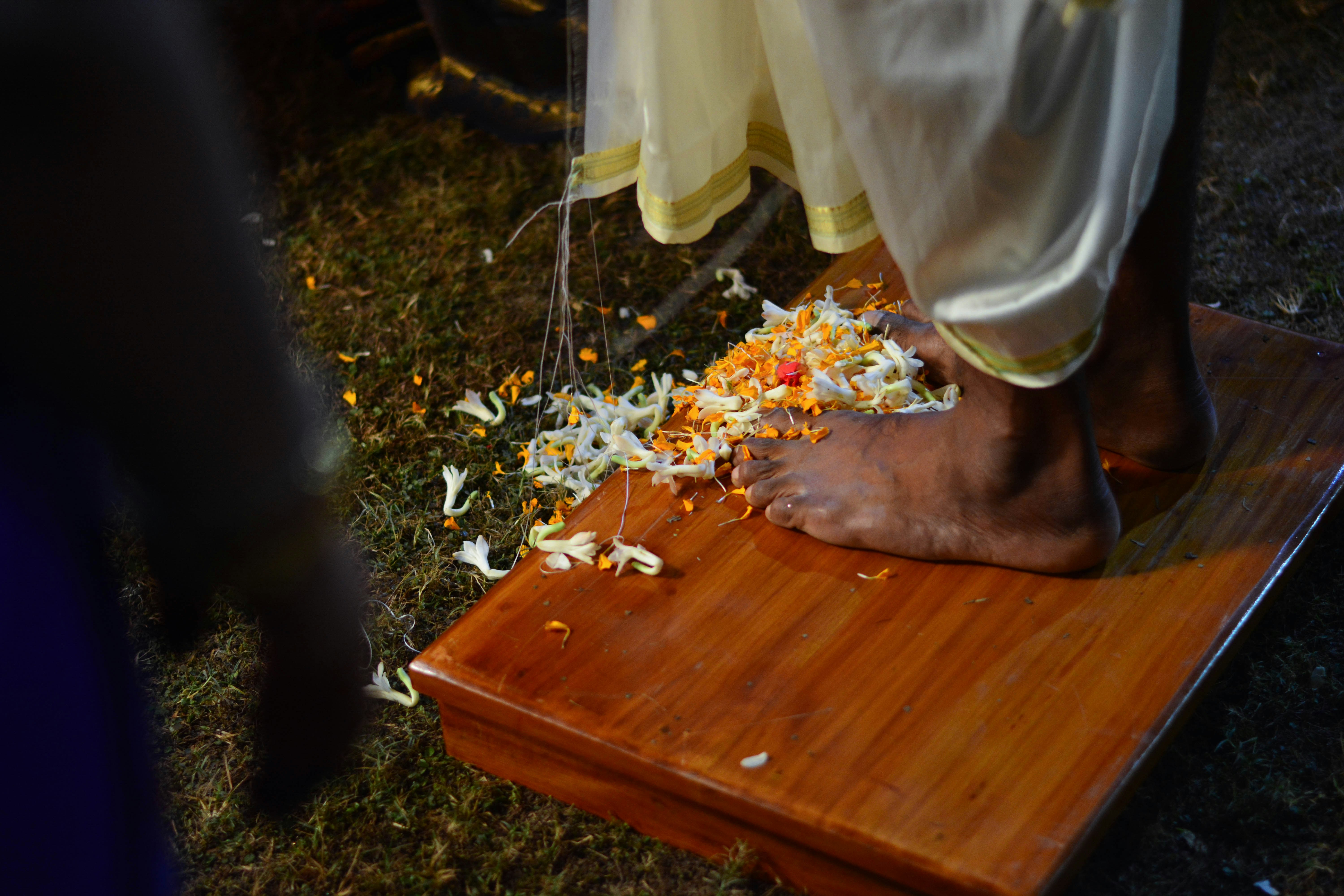 a person standing on top of a wooden cutting board, Flowers lain at the feet of a bridegroom during a Bengali wedding ceremony in West Bengal, India. 