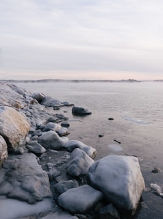 a rocky beach covered in snow next to a body of water