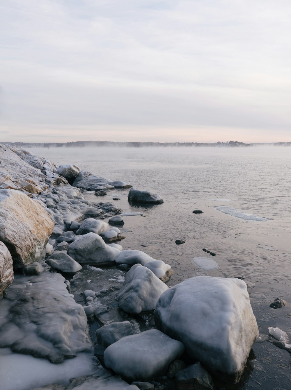 a rocky beach covered in snow next to a body of water