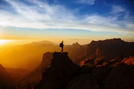 A lone trekker silhouetted against the rising sun atop a mountain summit, embracing the quiet.