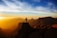 A smiling hiker standing on a rocky peak overlooking a vast, rugged mountain range at sunset.