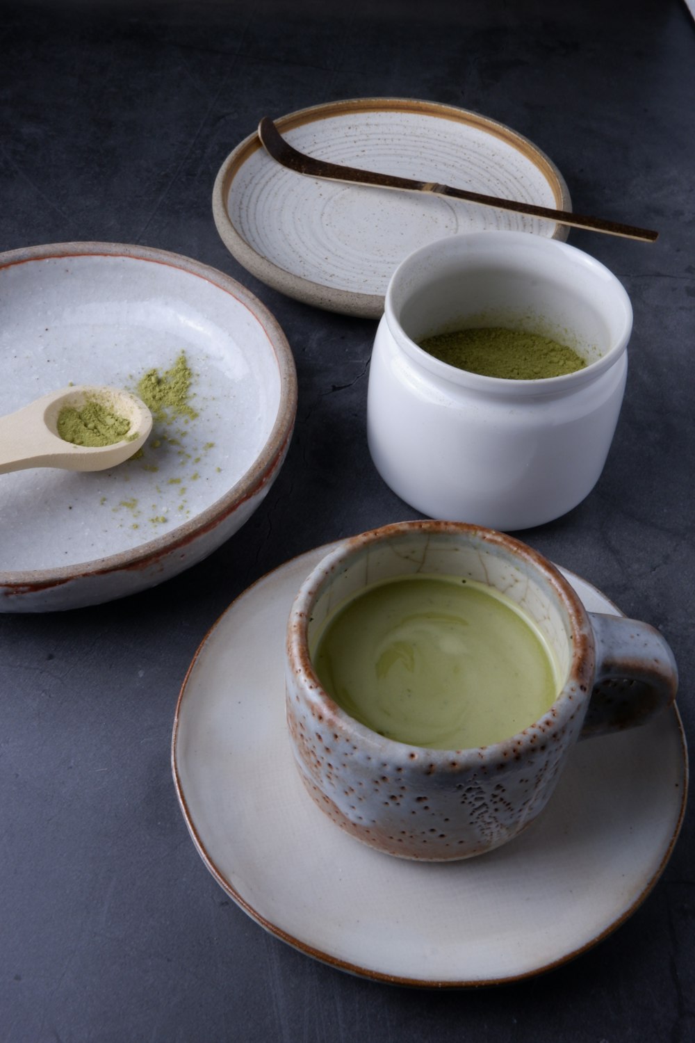 a cup of green tea next to a plate with a spoon