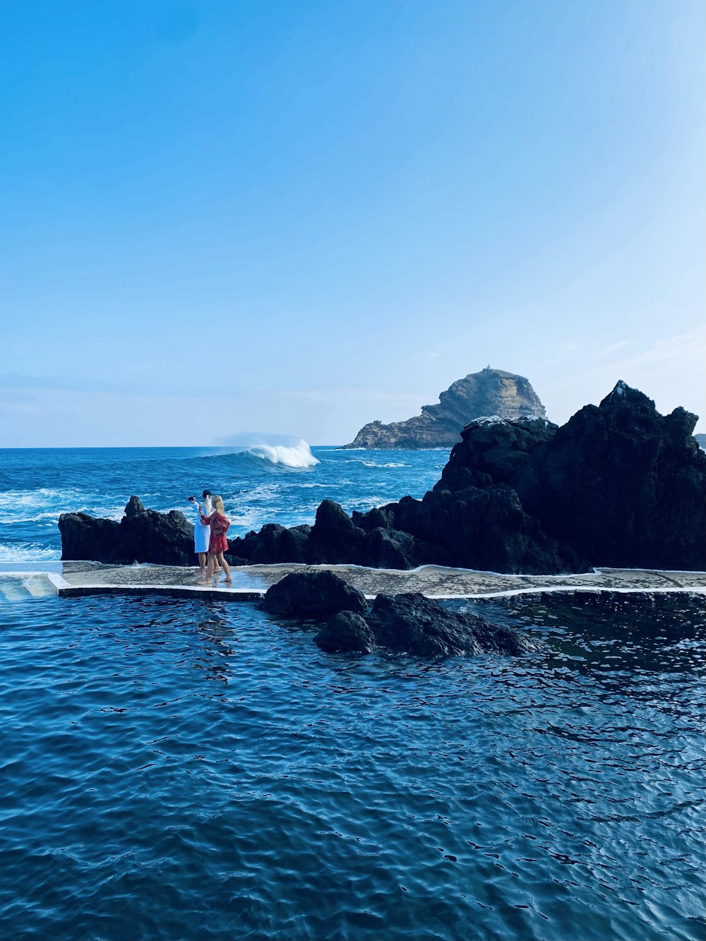 two people standing on a rock in the ocean