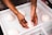 Hands of a person shaping or handling dough balls on a white surface. The person has a tattoo on their forearm.