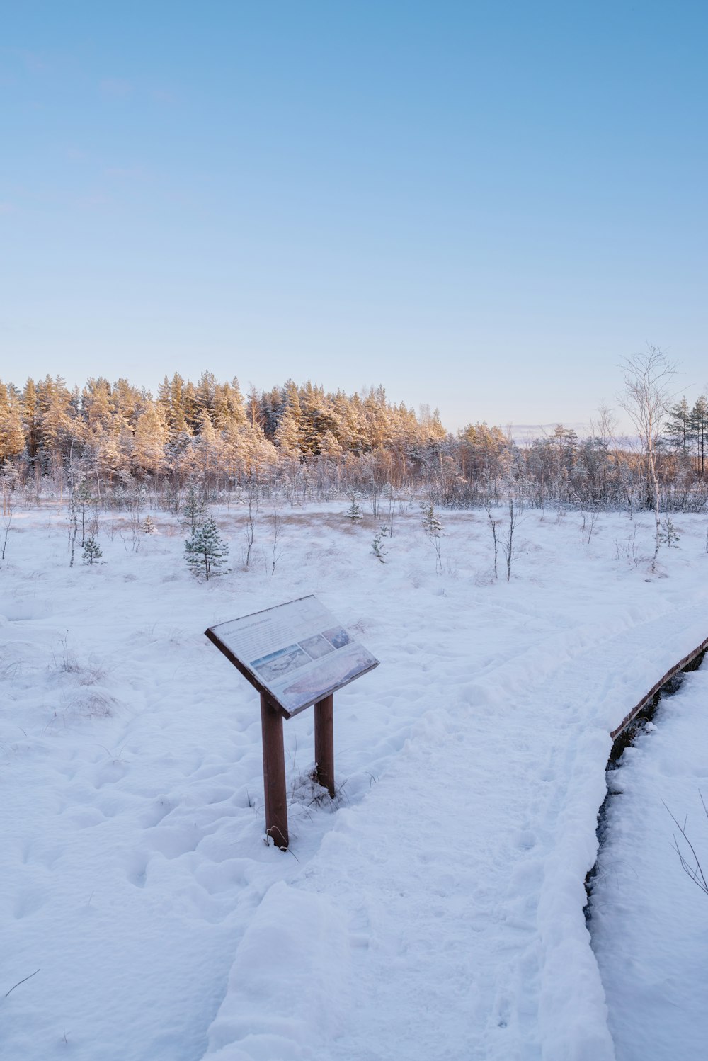 a wooden bench sitting in the middle of a snow covered field