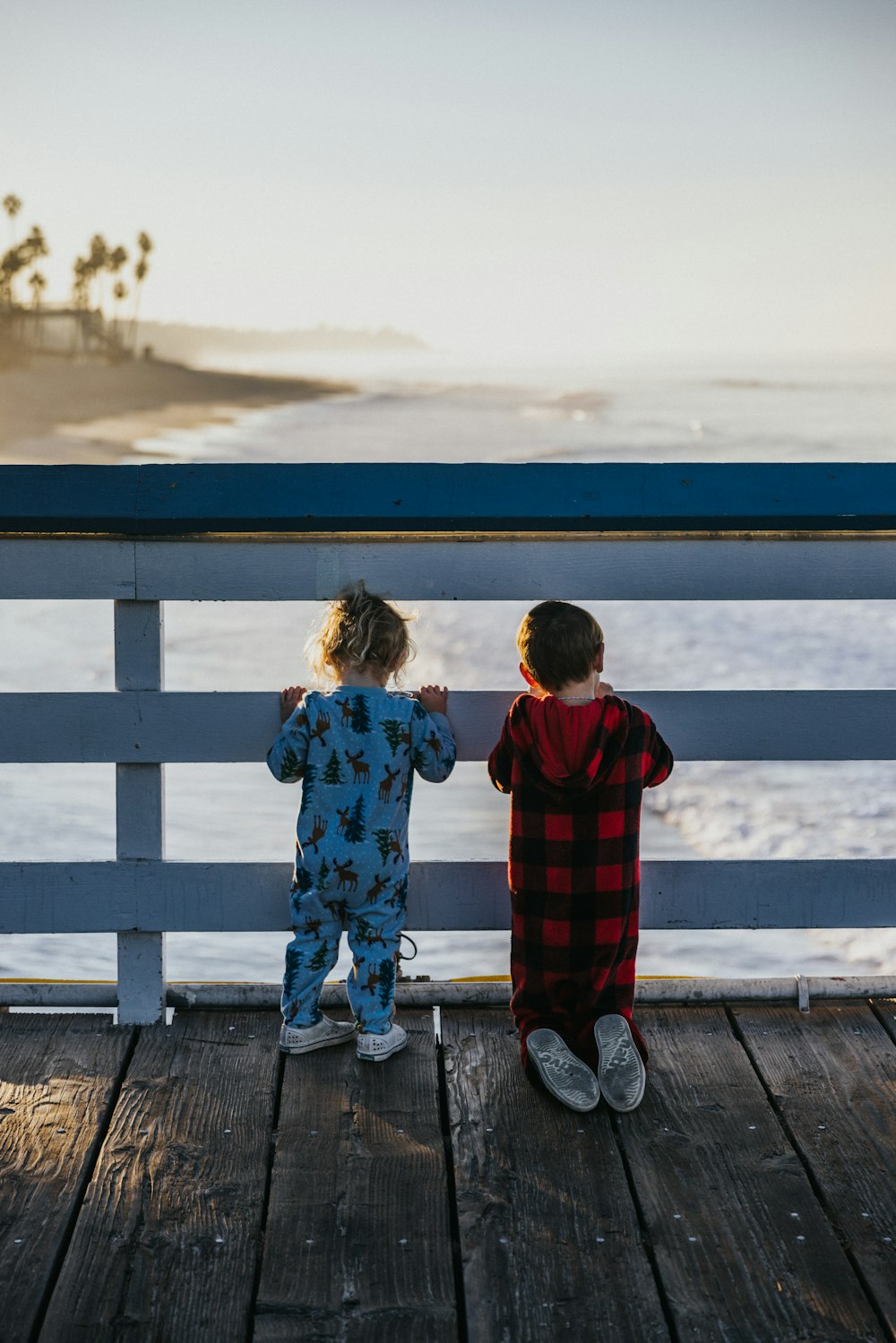two children standing on a deck looking out at the ocean