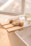 A serene spa-like setting with a wooden bath tray placed across a bathtub. The tray holds a loofah, a textured cloth, a natural bristle brush, a small bowl, and a glass candle. The soft lighting and neutral color scheme enhance the calming ambiance.
