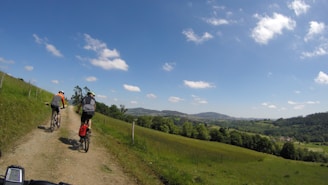 Cyclists riding rail bikes through lush green hills under a bright blue sky in Suisse Normande.