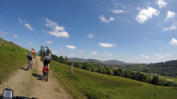 Cyclists riding rail bikes through lush green hills under a bright blue sky in Suisse Normande.