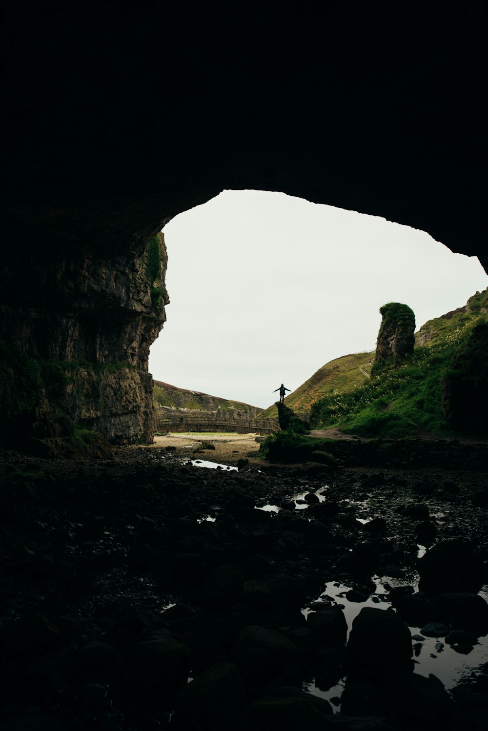 a person standing in a cave looking out at the water
