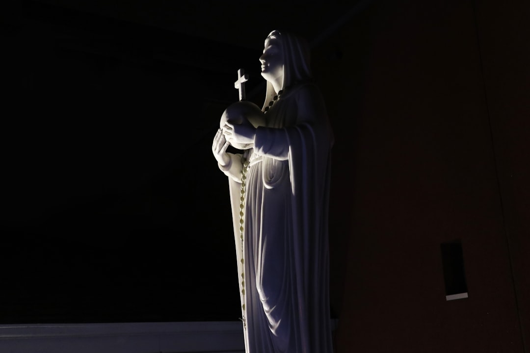 a statue of a woman holding a cross in a dark room, One of two statues outside St. Rose of Lima Parish in Scarborough.