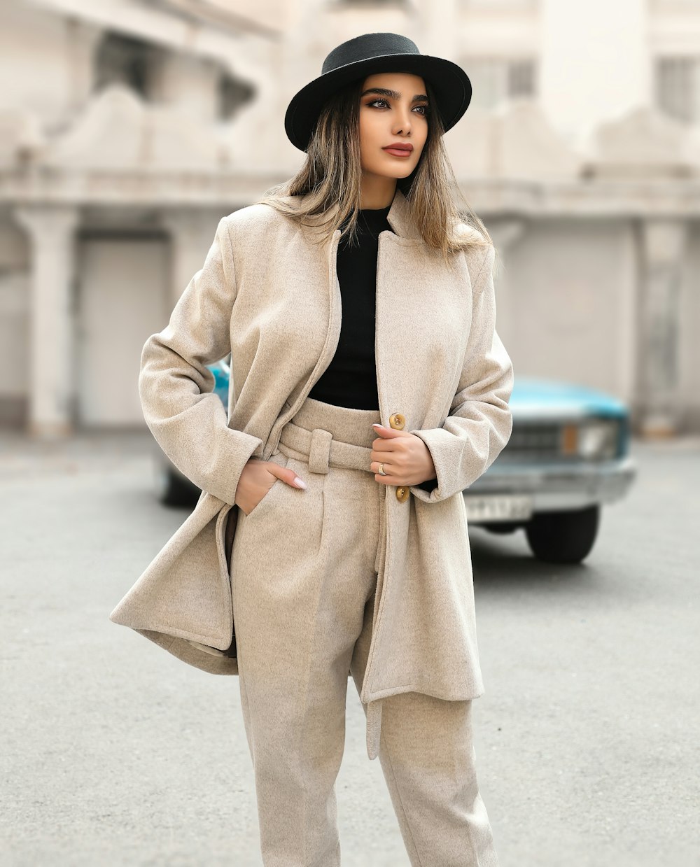 a woman in a hat and coat standing in a parking lot