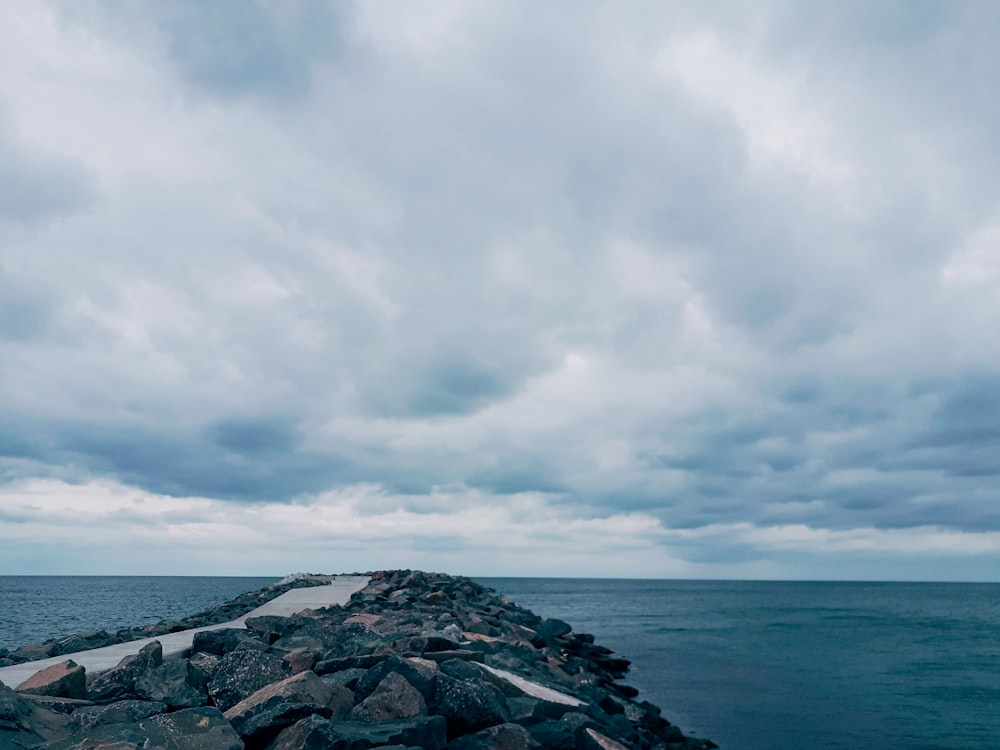 a long stone wall stretches out into the ocean under a cloudy sky