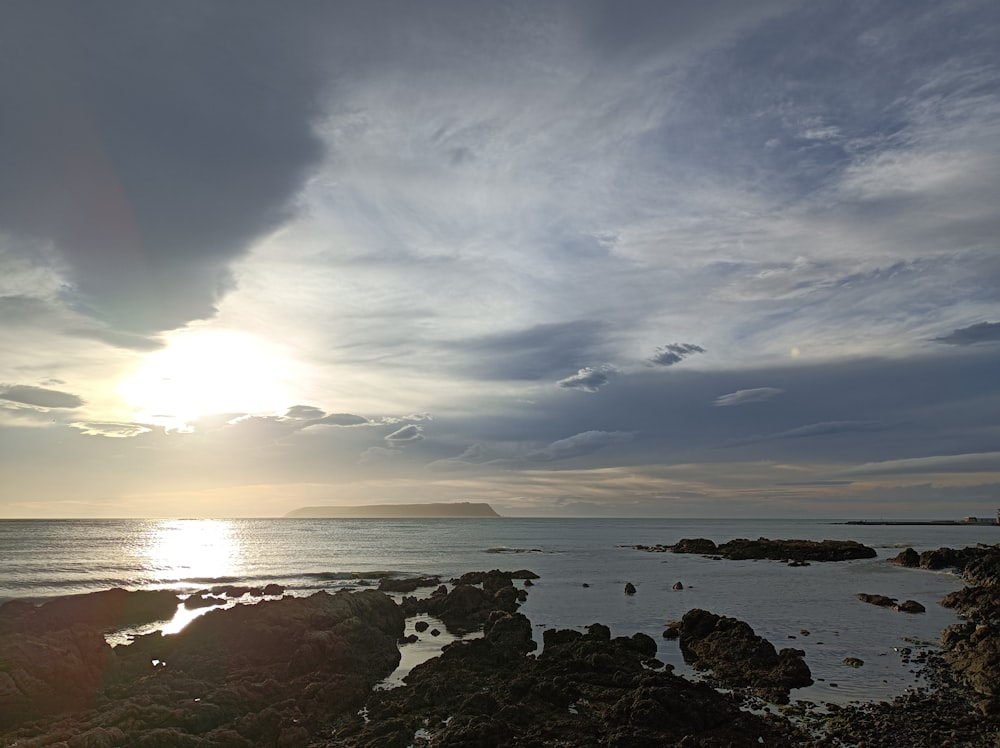 the sun is setting over a rocky beach