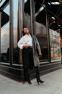 A stylish man in a casual black shirt and jeans leaning against a modern building