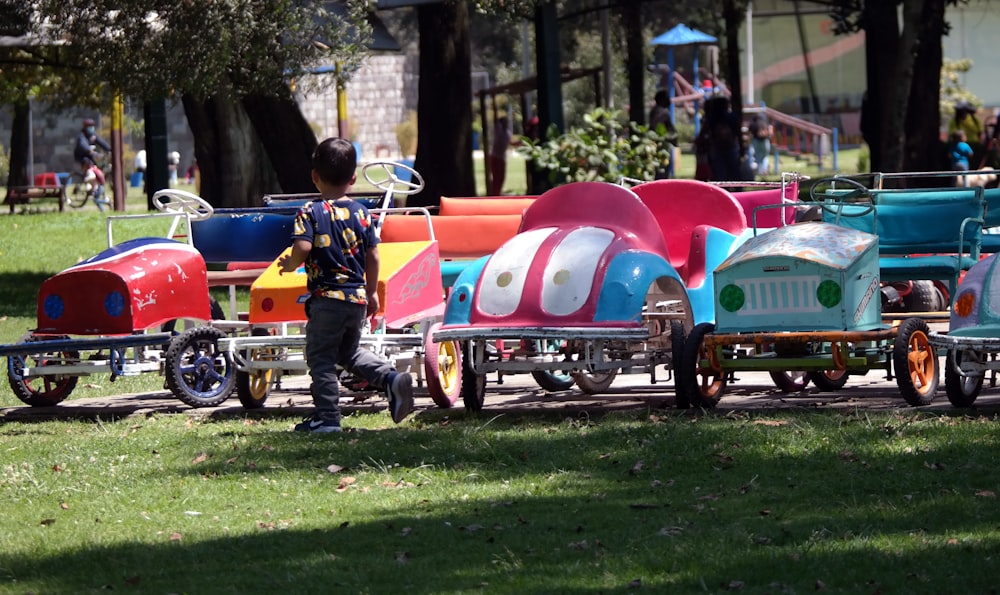 a little boy standing next to a row of colorful toy cars