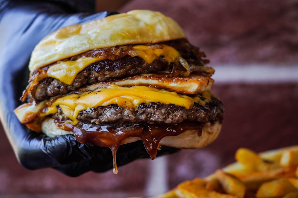 a hand holding a cheeseburger over a pile of french fries