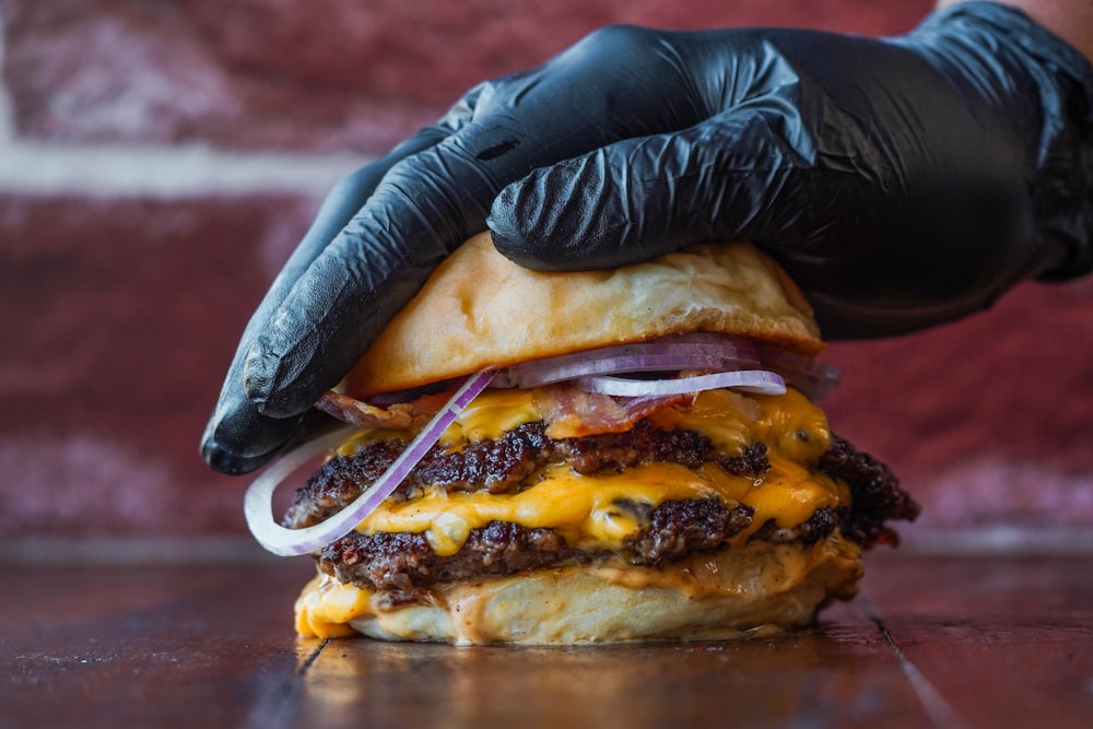 a hand in a glove holding a cheeseburger