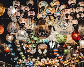 A vast array of colorful mosaic lamps hanging from the ceiling, each displaying intricate and diverse patterns. The setting suggests an artisanal marketplace or a specialty lighting store, with a warm and inviting atmosphere.