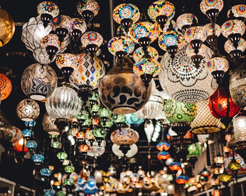 A vast array of colorful mosaic lamps hanging from the ceiling, each displaying intricate and diverse patterns. The setting suggests an artisanal marketplace or a specialty lighting store, with a warm and inviting atmosphere.