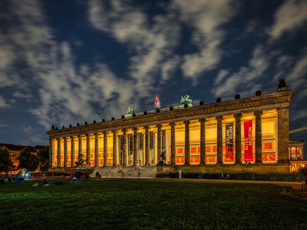 a large building lit up at night with clouds in the sky
