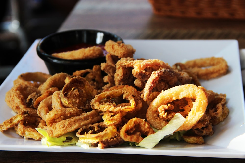 a white plate topped with onion rings and a bowl of dipping sauce