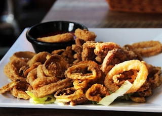 a white plate topped with onion rings and a bowl of dipping sauce