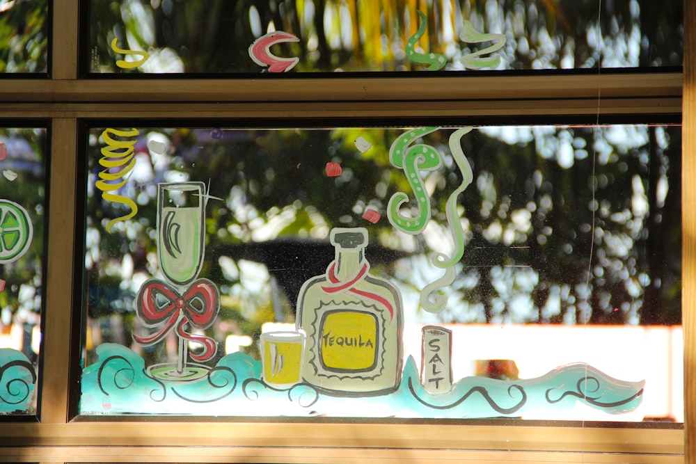 a window with a bottle of alcohol and a cup on it