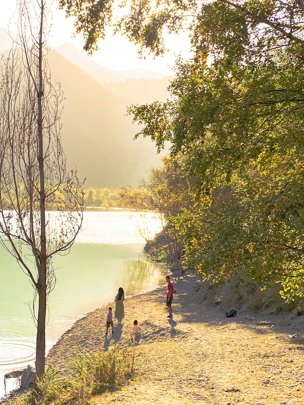 a group of people walking down a dirt road next to a body of water