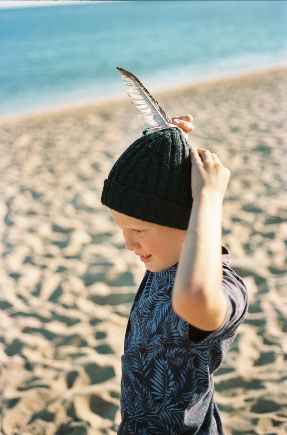 a young boy on the beach with a feather on his head
