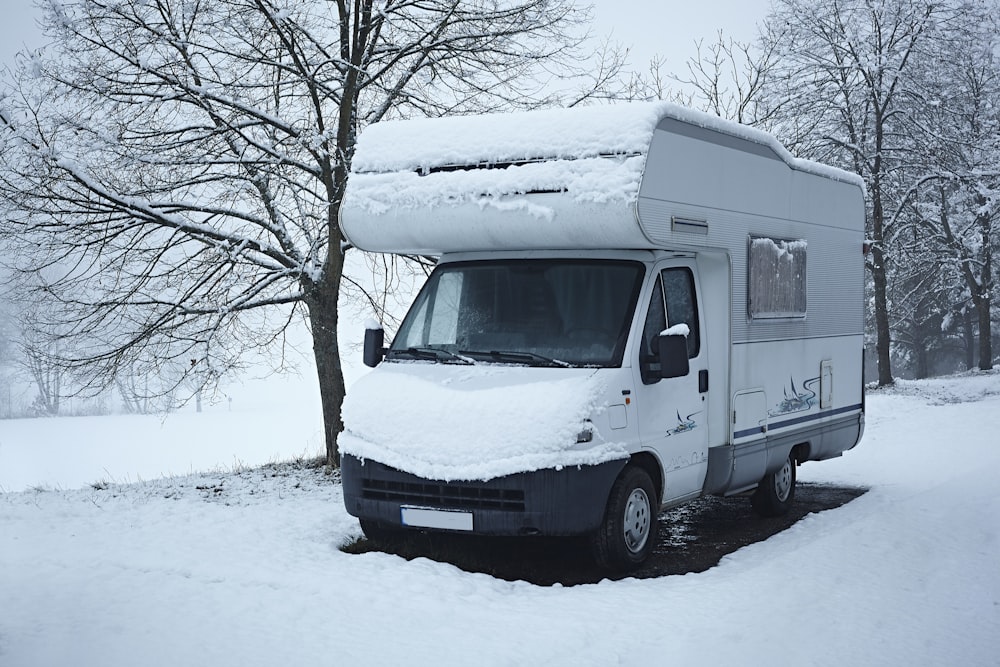 a white van covered in snow next to a tree