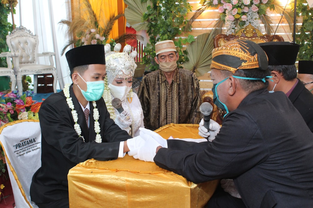 a group of men sitting around a table wearing masks