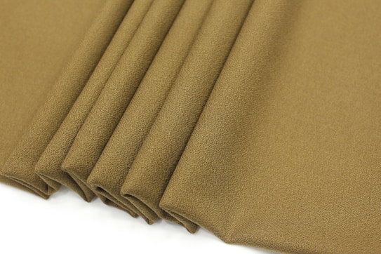 Several folds of fabric in a textured, olive green material appear neatly arranged. The fabric displays a soft, matte appearance with a subtle grain pattern.