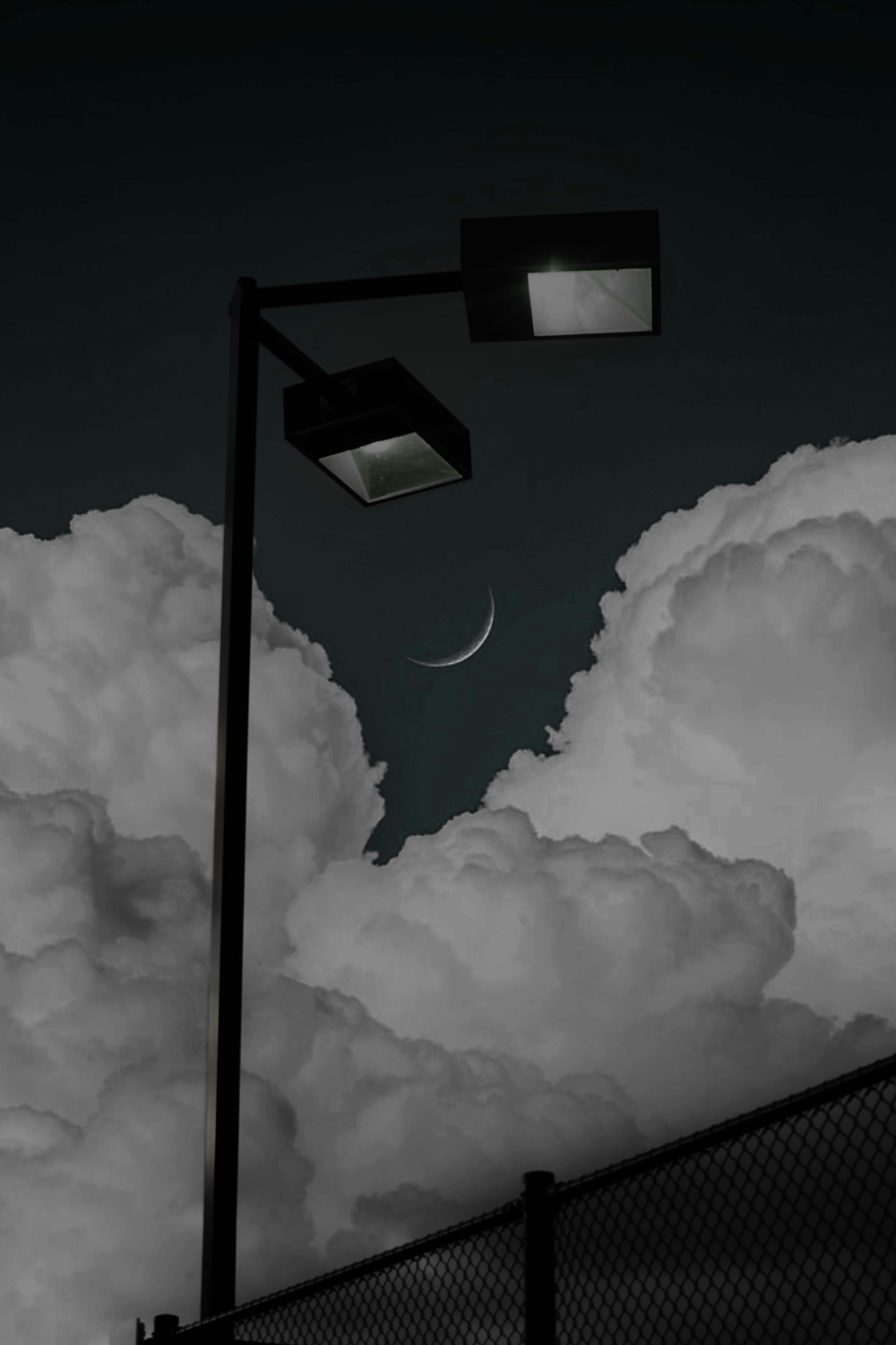 a black and white photo of a street light and clouds