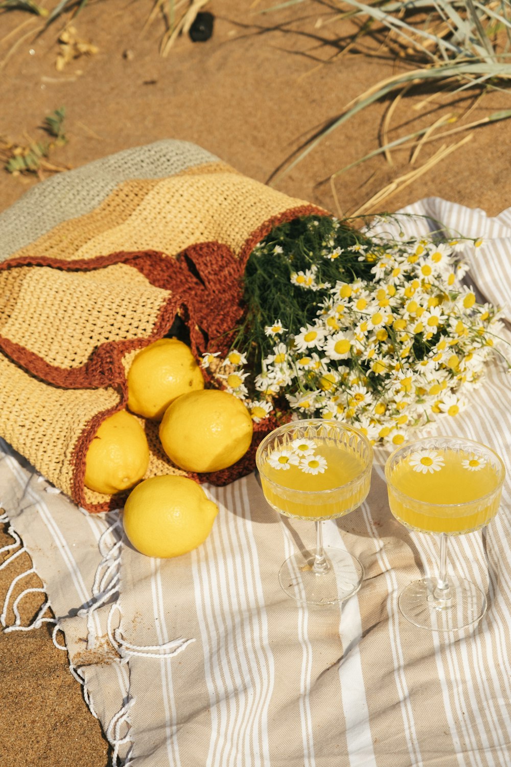 a towel, two glasses of lemonade, and a bunch of daisies on