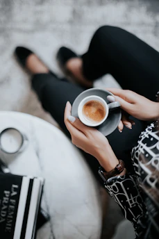 A chic woman in an elegant, soft beige jumpsuit sitting at a stylish coffee shop table with a warm latte.