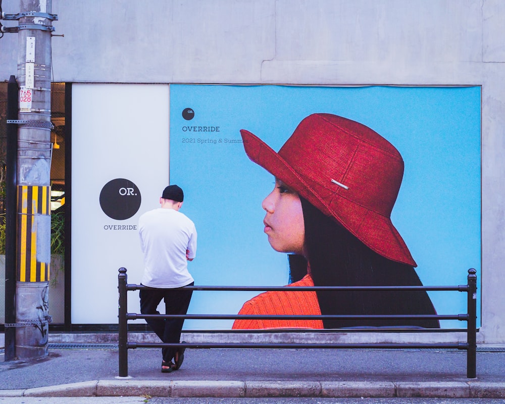 a man walking past a large advertisement of a woman wearing a red hat