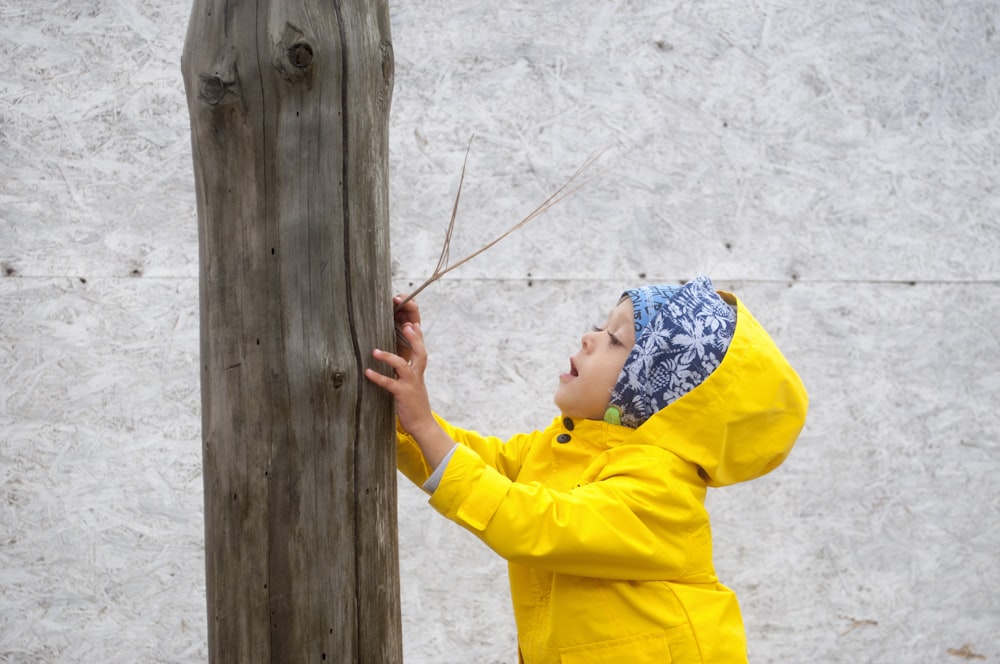 a little girl in a yellow rain coat holding a stick