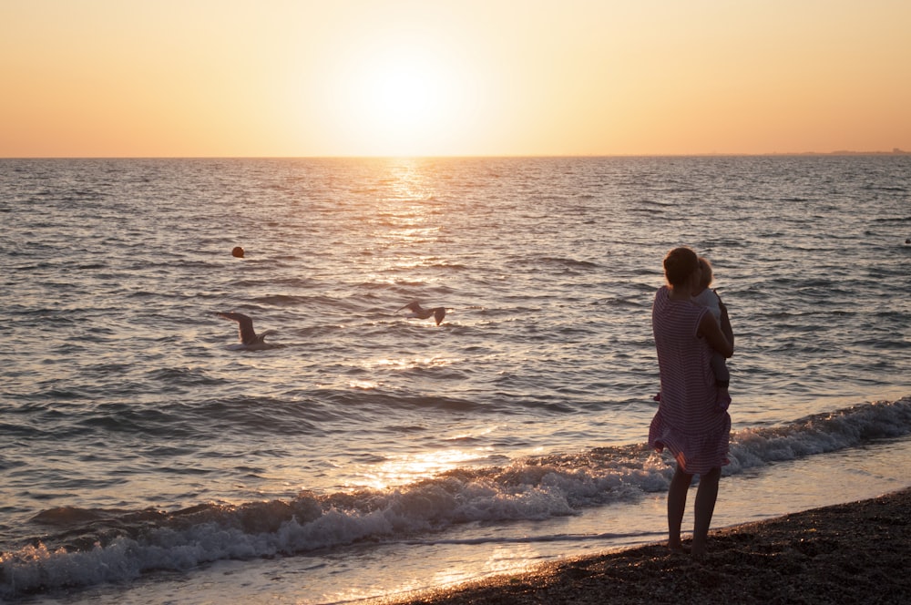 Una mujer parada en una playa mirando la puesta de sol