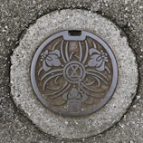Manhole cover with a geometric pattern resting on a paved road.