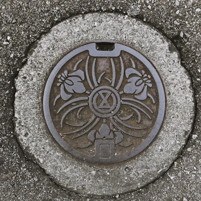 Manhole cover with a geometric pattern resting on a paved road.