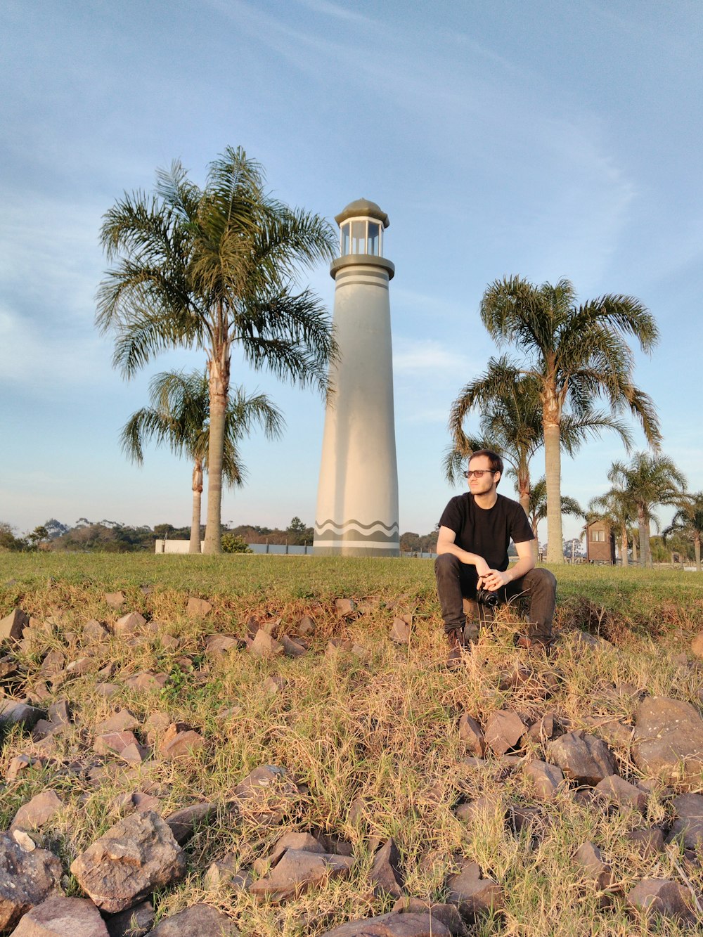 a man sitting in a field next to a light house