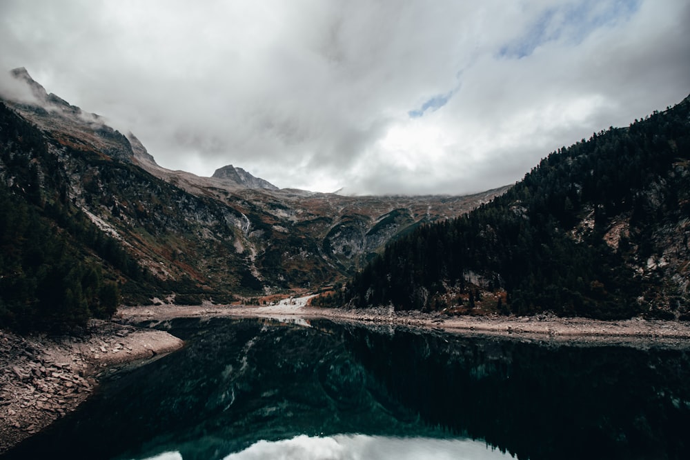 a body of water surrounded by mountains under a cloudy sky