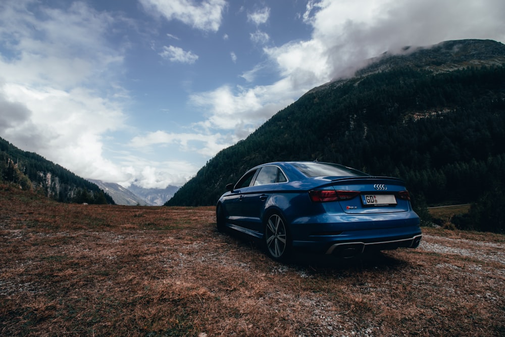 a blue car parked on a dirt road in front of a mountain