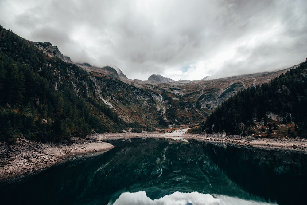 a body of water surrounded by mountains under a cloudy sky