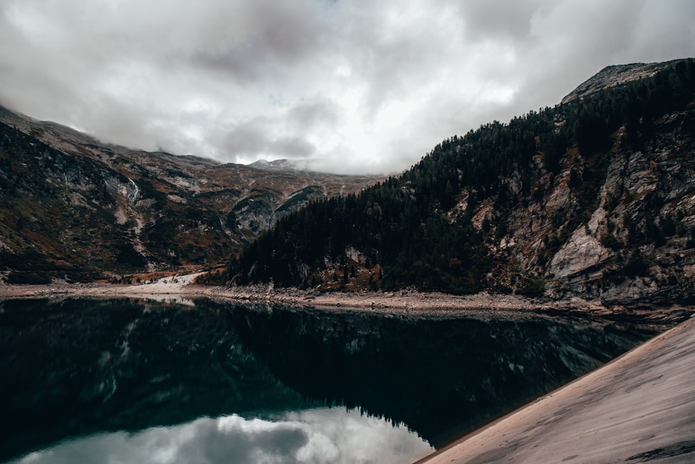 a body of water surrounded by mountains under a cloudy sky