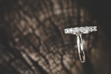 A silver-colored ring adorned with multiple small diamonds resting on a dark and textured wood surface, creating a contrast between the sparkling jewels and the natural background.