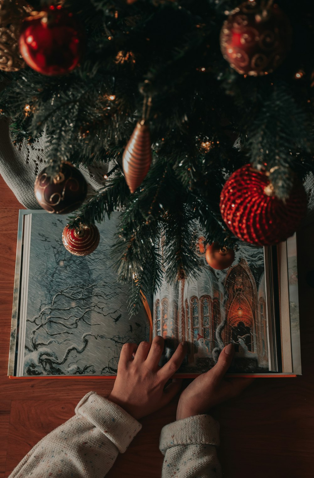 人がクリスマスツリーの下で本を読んでいる